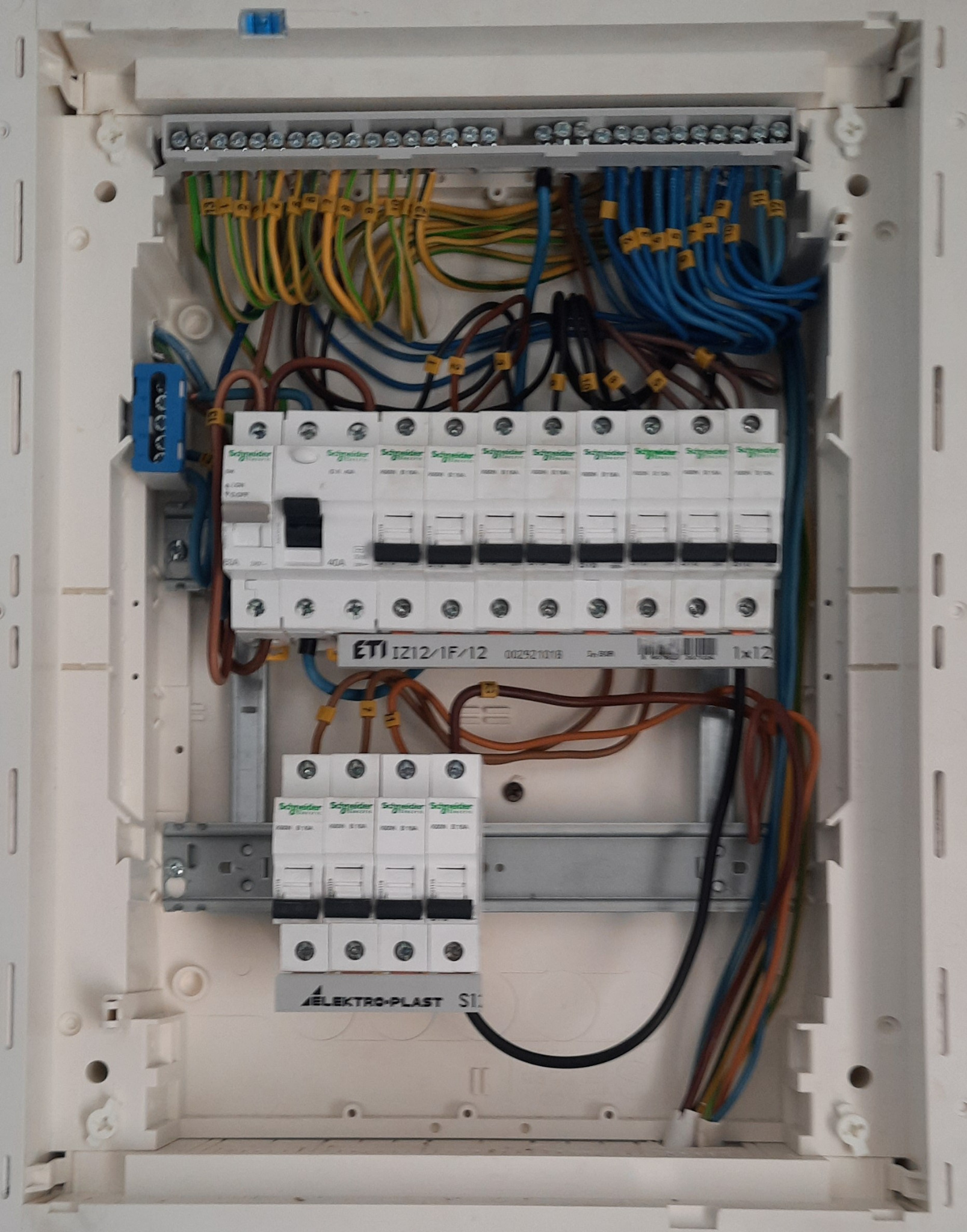 Otwarta skrzynka elektryczna z zainstalowanymi bezpiecznikami, przewodami oznaczonymi numerami i listwami zaciskowymi, widoczna tabliczka ETI IZ12/1F/12 i logo Elektro-Plast.