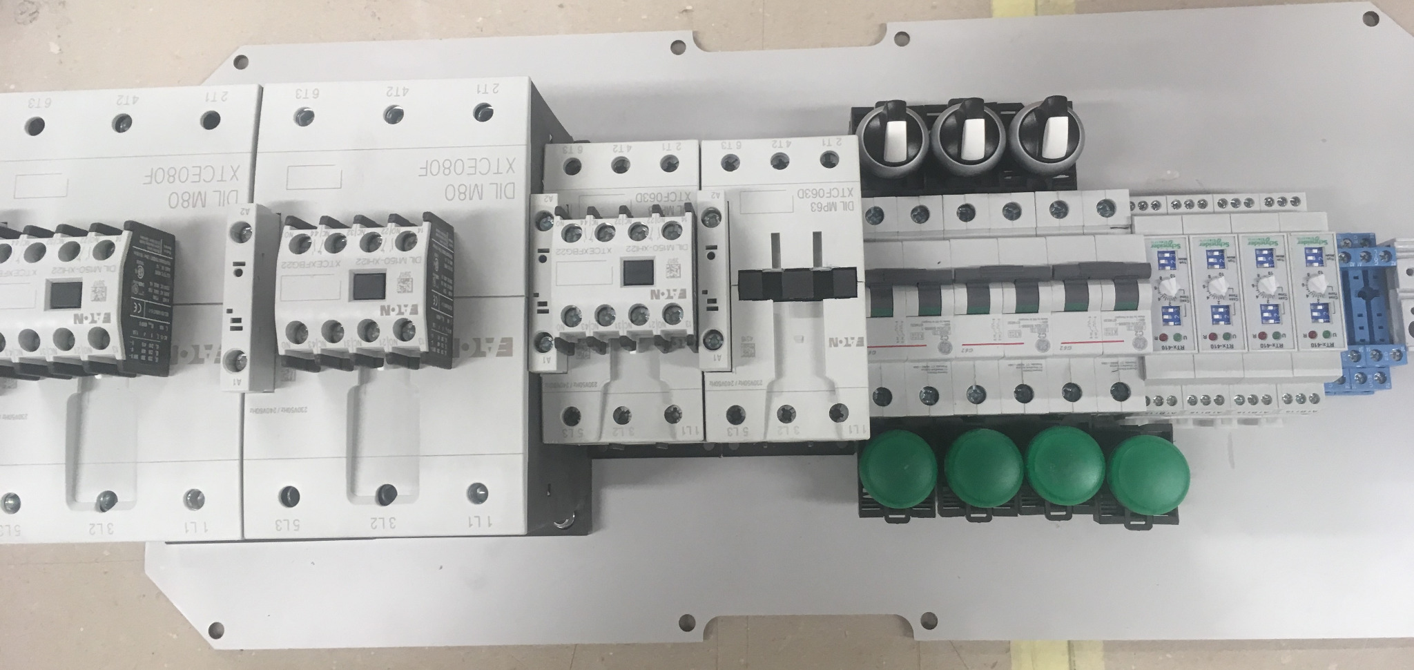 Rozdzielnica elektryczna z zamontowanymi stycznikami Eaton, wyłącznikami różnicowoprądowymi, bezpiecznikami i zielonymi przyciskami, widok z góry.