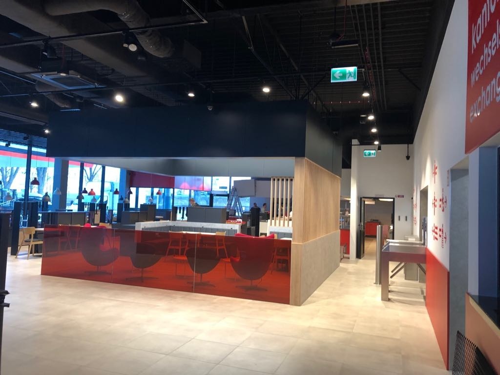 Wnętrze stacji paliw Citronex Zgorzelec z czerwonymi elementami dekoracyjnymi, widoczne krzesła, stoły, przeszklenia oraz fragmenty instalacji sufitowej.