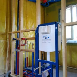 Szkielet instalacji wodnej w trakcie montażu w Głosce, widoczne niebieskie rury doprowadzające wodę, czerwone rury odprowadzające oraz stelaż podtynkowy do WC firmy Sanit.