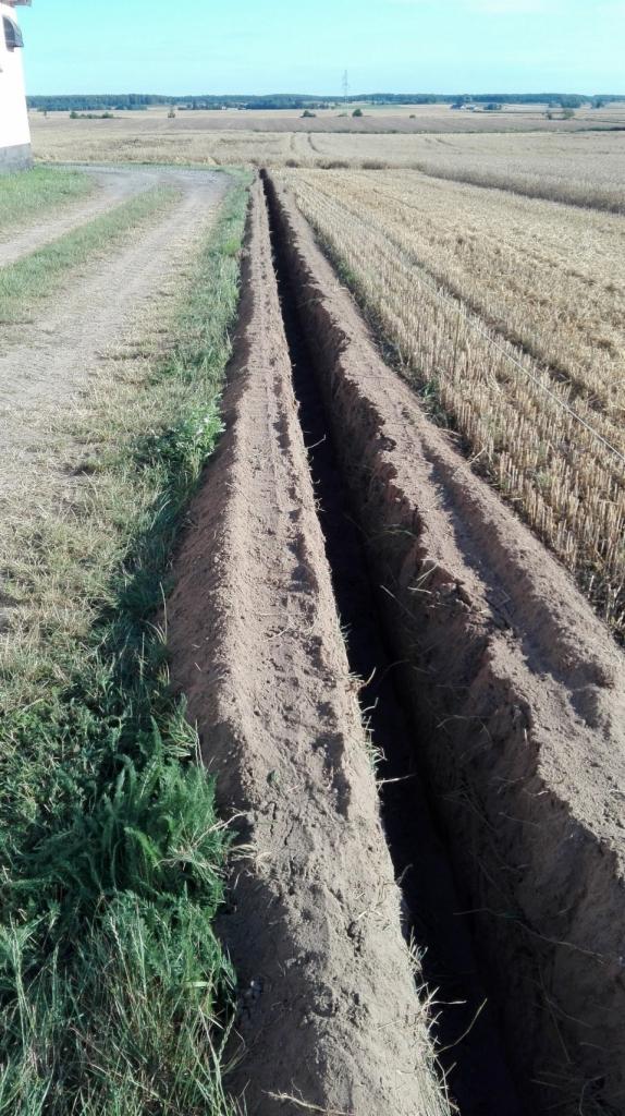 Długi, wąski wykop w ziemi, biegnący przez pole ze ściętym zbożem, widok z góry na świeżo wykopany rów.