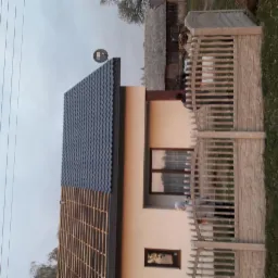 Dom jednorodzinny z częściowo nowym, grafitowym dachem z blachodachówki trapezowej, widoczne drewniane łaty pod pokryciem, w tle ogrodzenie z prefabrykatów betonowych.