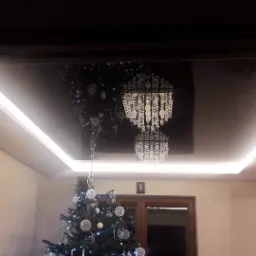 Salon z czarnym, błyszczącym sufitem podwieszanym, oświetleniem LED i kryształowym żyrandolem, udekorowany choinką.