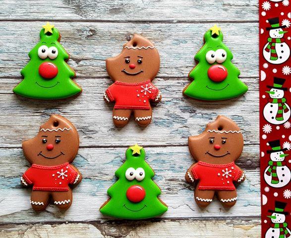 Ręcznie robione, świąteczne pierniczki: choinki z czerwonymi nosami i piernikowi ludziki w czerwonych sweterkach ze śnieżynkami, ułożone na drewnianym tle z dekoracyjnym paskiem z bałwankami.