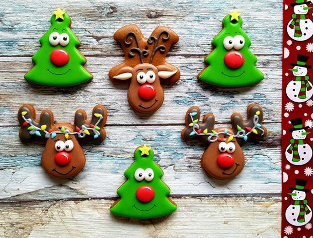 Świąteczne pierniczki: trzy renifery z lukrowanymi rogami-lampkami i dwa choinkowe z czerwonymi nosami, ułożone na drewnianym tle z efektem postarzenia, obok dekoracyjna bordiura z bałwankami.