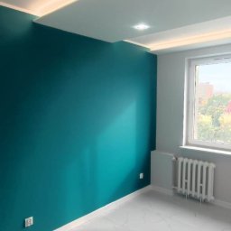 F.P.H.U. ROMEX - Pomalowane na turkusowo ściany i biała marmurowa podłoga w pustym pokoju z oknem. Sufit podwieszany z oświetleniem LED. Grzejnik w kolorze szarym.