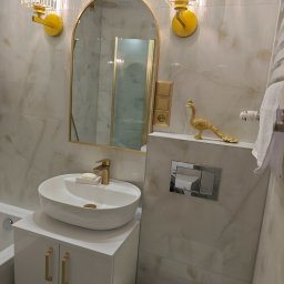 Firma Produkcyjno-Handlowo-Usługowa ROMEX Alicja Niezgoda - Elegancka łazienka z umywalką nablatową, złotymi akcentami (armatura, oświetlenie, dekoracja pawia) i marmurowymi płytkami. Nowoczesny design z dbałością o detale.