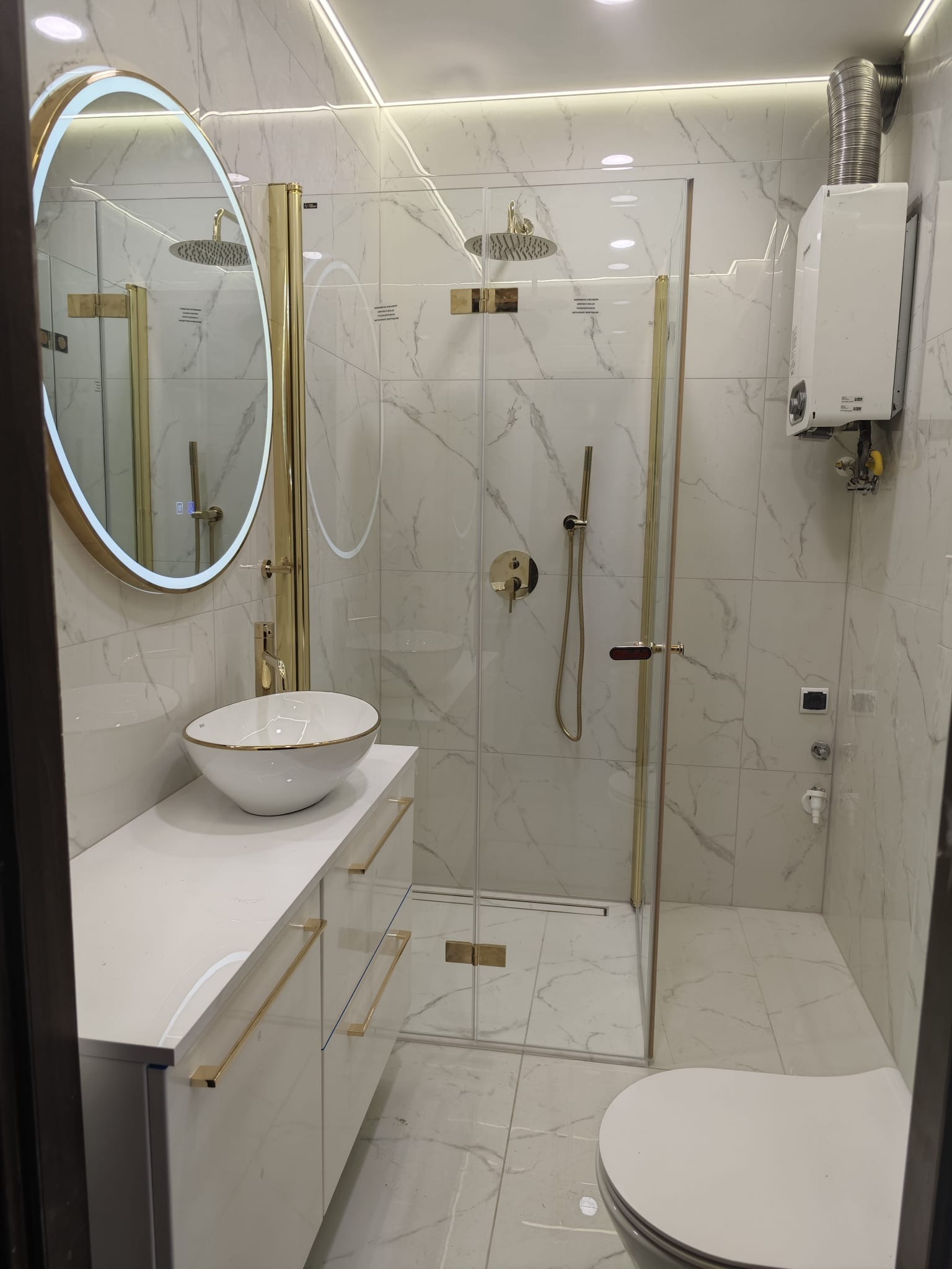 Elegancka łazienka z kabiną prysznicową typu walk-in, umywalką nablatową z szafką i okrągłym lustrem z podświetleniem LED, wykończona marmurem.