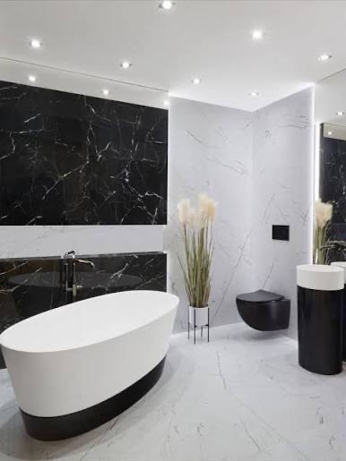 Nowoczesna łazienka z wolnostojącą wanną, czarną armaturą i marmurowymi płytkami na ścianach. Minimalistyczny design z akcentem roślinnym.