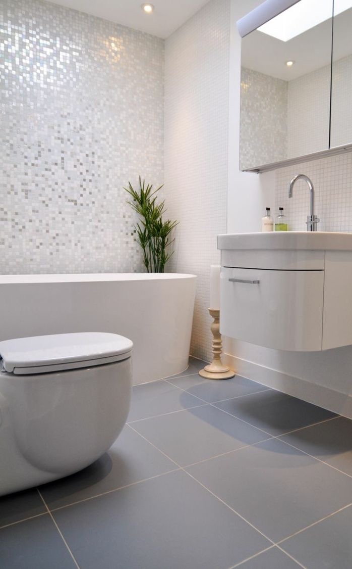 Nowoczesna łazienka z mozaiką, białą wanną i szafką umywalkową. Szare płytki podłogowe i roślina doniczkowa dodają elegancji. Oświetlenie punktowe.
