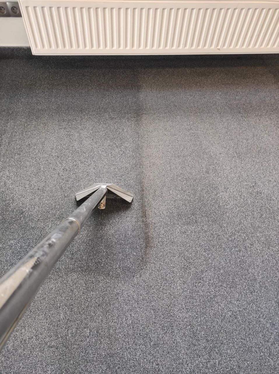 Szary dywan czyszczony odkurzaczem piorącym, widoczny ślad po czyszczeniu, grzejnik na ścianie w tle.