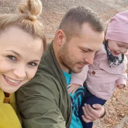 Rodzinne selfie w Koninie: uśmiechnięta kobieta w żółtym swetrze, mężczyzna z brodą trzymający na rękach roześmianą dziewczynkę w różowej kurtce i czapce.