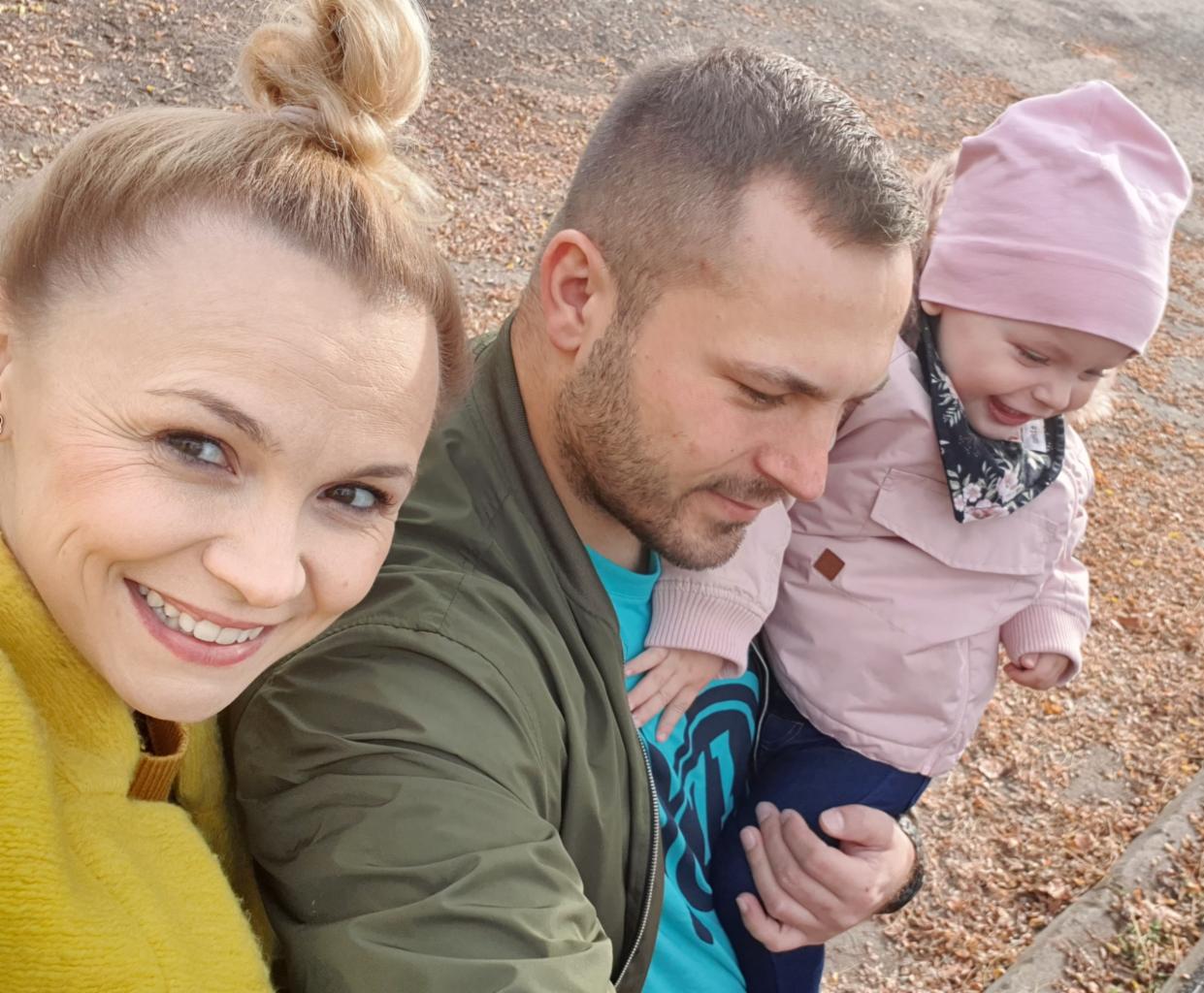 Rodzinne selfie w Koninie: uśmiechnięta kobieta w żółtym swetrze, mężczyzna z brodą trzymający na rękach roześmianą dziewczynkę w różowej kurtce i czapce.