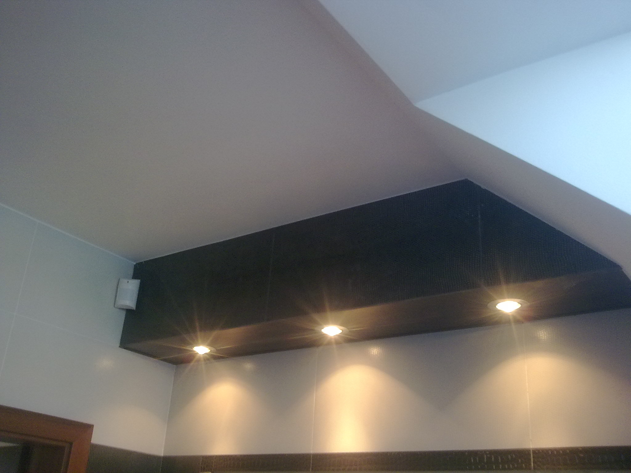 Wykończona łazienka w Rumi z podwieszanym sufitem z punktowym oświetleniem LED, szare płytki na ścianach i ciemny pas dekoracyjny u dołu.