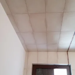 Beżowe płytki kwadratowe na ścianie i suficie łazienki, z brązowymi dekoracyjnymi pasami, widok z dołu na fragment ściany i okno.