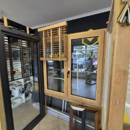 Ekspozycja okien PCV i aluminiowych z drewnianymi żaluzjami w salonie w Nowej Soli, widoczne różne ramy okienne i profile.