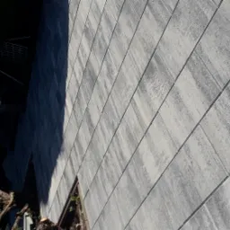 Nowa, szara nawierzchnia z prostokątnych płyt betonowych, ułożonych regularnie, z widocznym cieniem drzewa i fragmentem zieleni w tle.