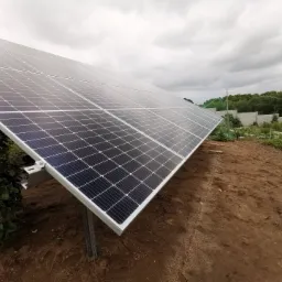 Instalacja fotowoltaiczna na gruncie, widoczna konstrukcja wsporcza z metalowymi profilami, tło pochmurne.