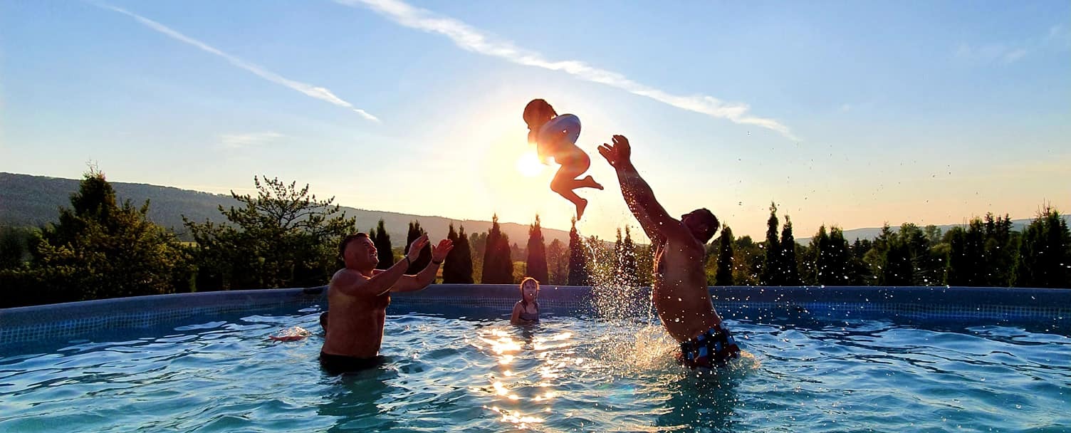 Radosny skok dziecka z kołem ratunkowym w ramiona ojca w basenie na tle zachodzącego słońca i krajobrazu.
