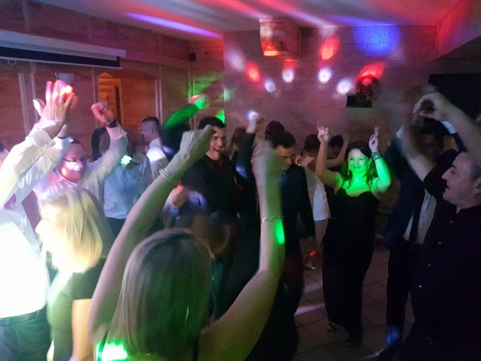 Roztańczony tłum ludzi w Ustrzykach Dolnych, w dyskotekowym oświetleniu podczas imprezy; widoczne podniesione ręce i uśmiechnięte twarze.