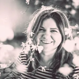 Uśmiechnięta kobieta w paski otoczona kwitnącymi gałązkami, portret w sepii z delikatnym rozmyciem tła i promieniami słońca.