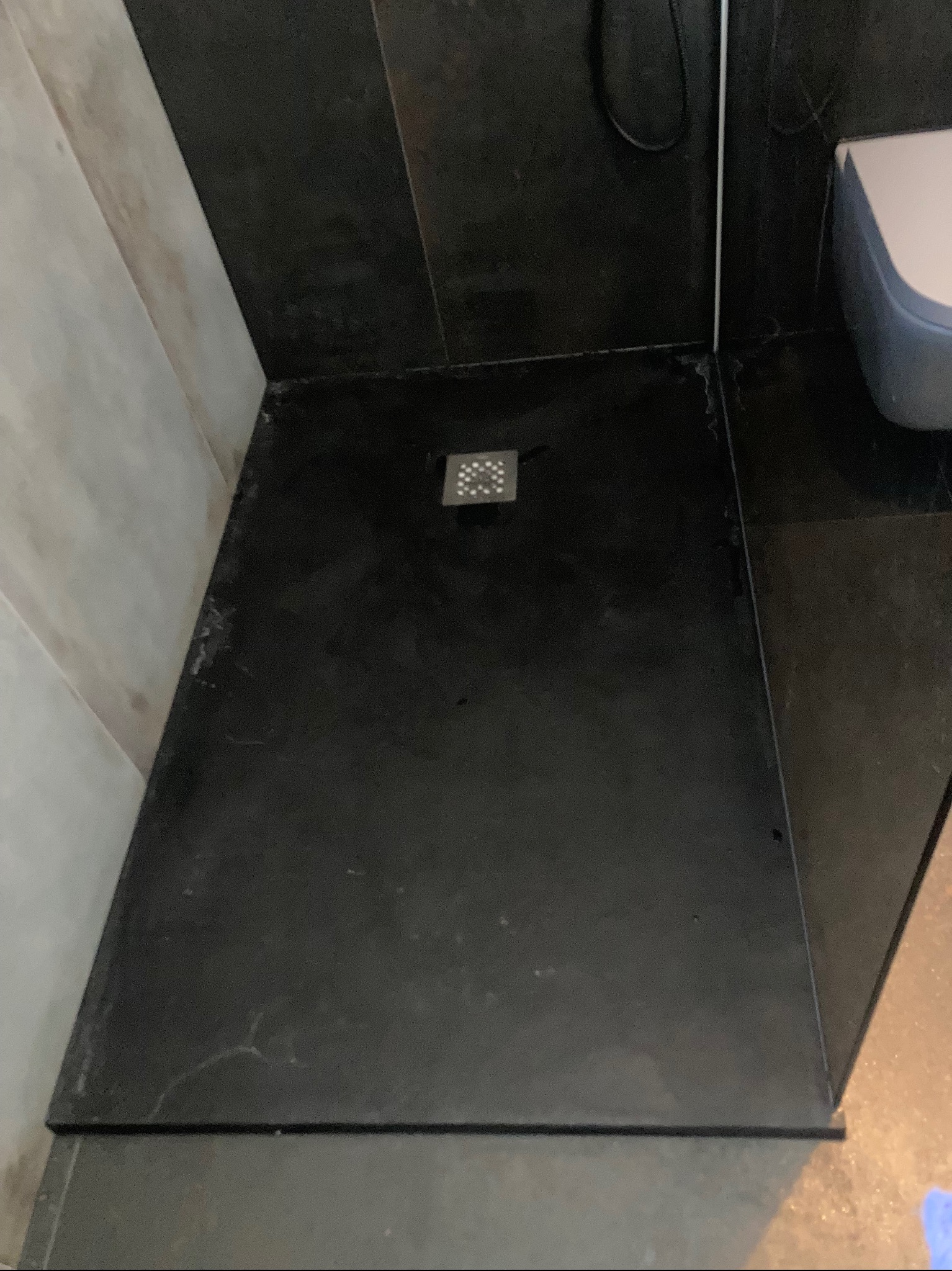 Nowoczesny brodzik z czarnych płytek w kabinie prysznicowej, widoczny odpływ liniowy i fragment toalety. Minimalistyczny design łazienki.