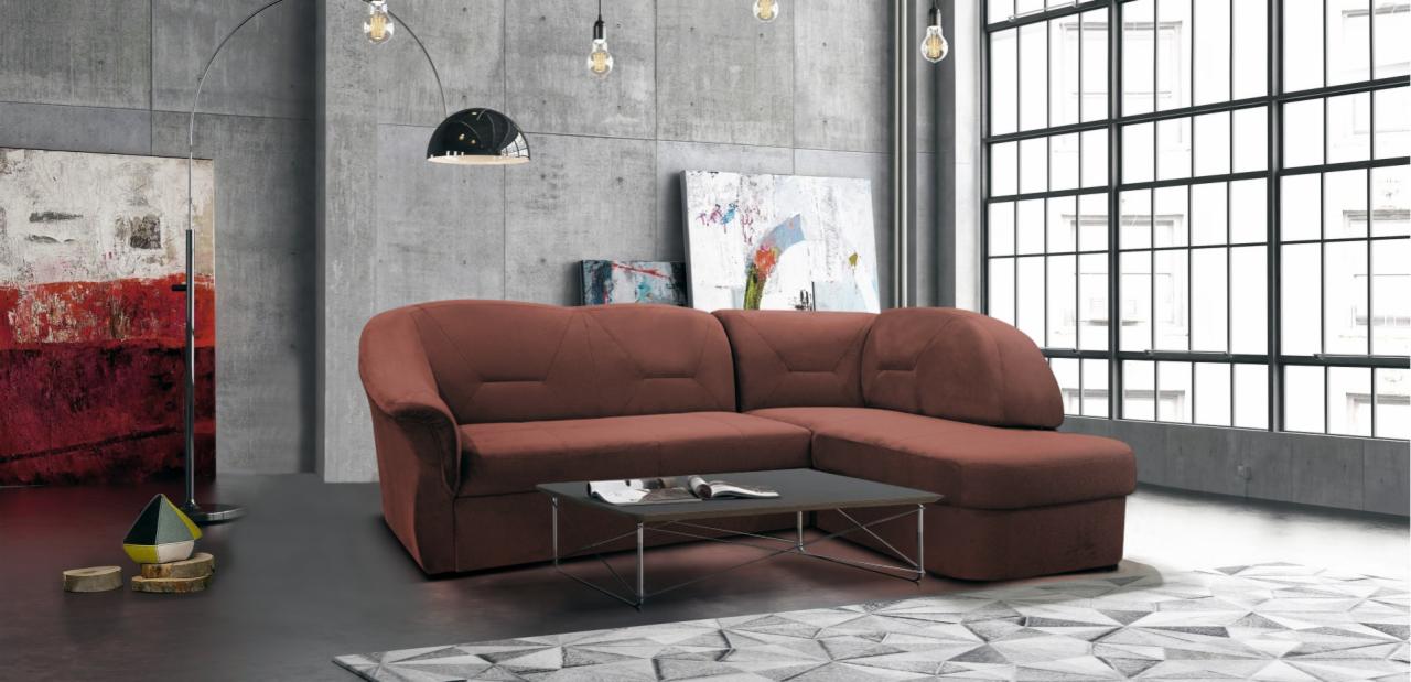 Brązowa, narożna sofa z geometrycznymi przeszyciami na oparciu, ustawiona w nowoczesnym wnętrzu z betonową ścianą i oknem w stylu industrialnym.