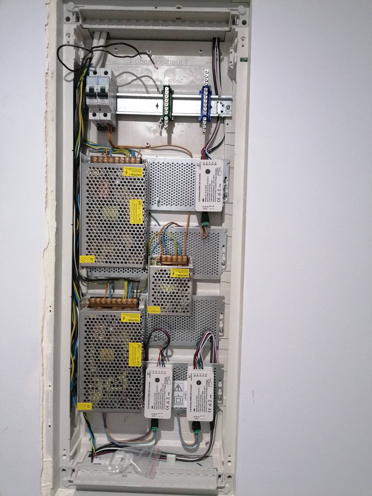 Wnętrze skrzynki elektrycznej z zainstalowanymi zasilaczami impulsowymi, bezpiecznikami i listwami zaciskowymi, widoczne przewody w różnych kolorach.