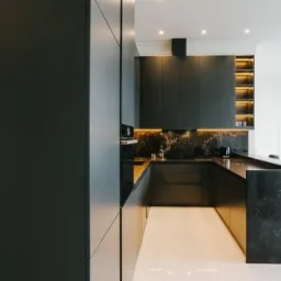 Nowoczesna kuchnia w odcieniach grafitu z marmurowym blatem i oświetleniem LED pod szafkami, biała podłoga z połyskiem, minimalistyczny design.