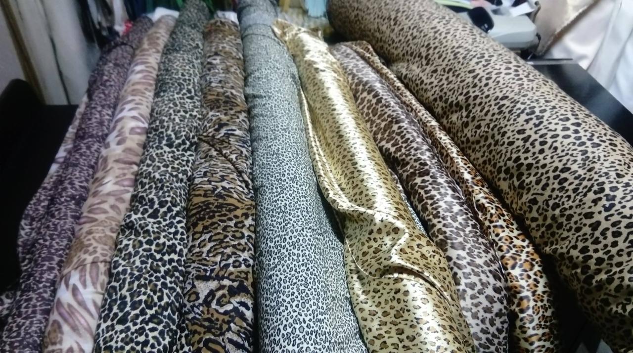Rzędy różnorodnych tkanin w panterkę, zwinięte w bele, ukazują bogatą paletę barw od ciemnych brązów po jasne beże i szarości, z różnymi rozmiarami cętek.