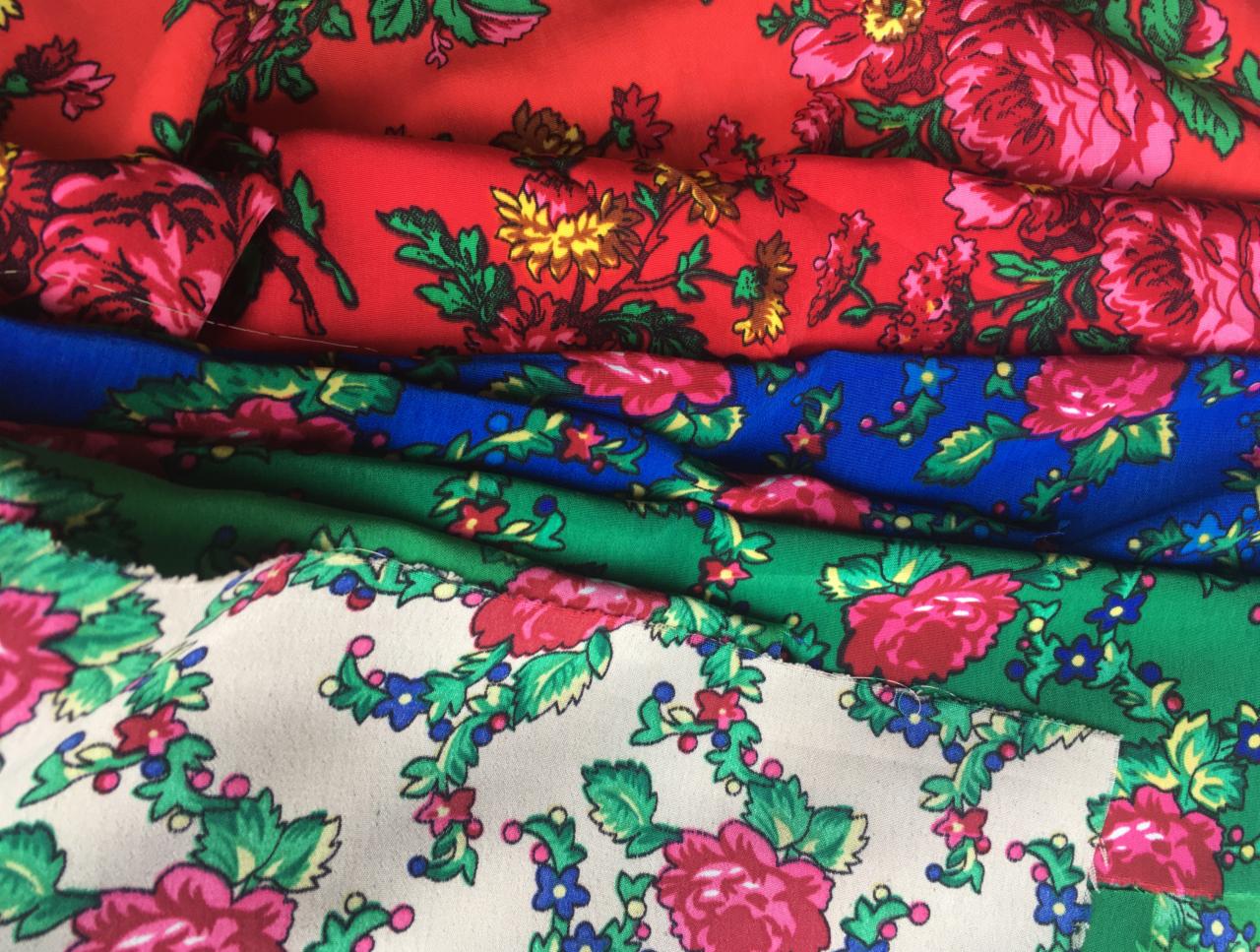 Stos pofałdowanych tkanin w kolorach czerwonym, niebieskim, zielonym i kremowym, z motywem róż i drobnych kwiatów.