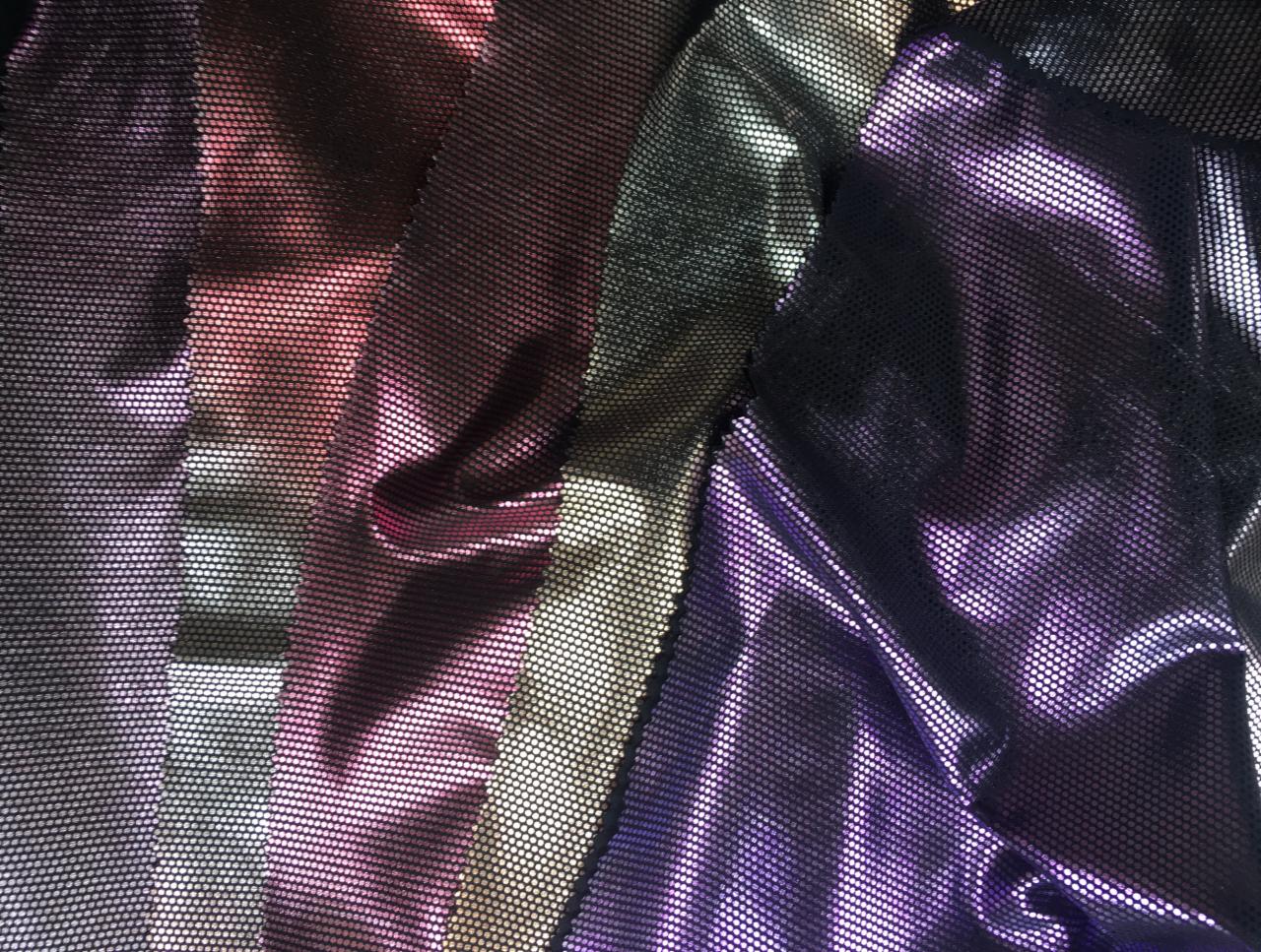 Połyskujące próbki tkanin siatkowych w odcieniach fioletu, czerwieni i złota, ułożone warstwami z widoczną strukturą oczek.