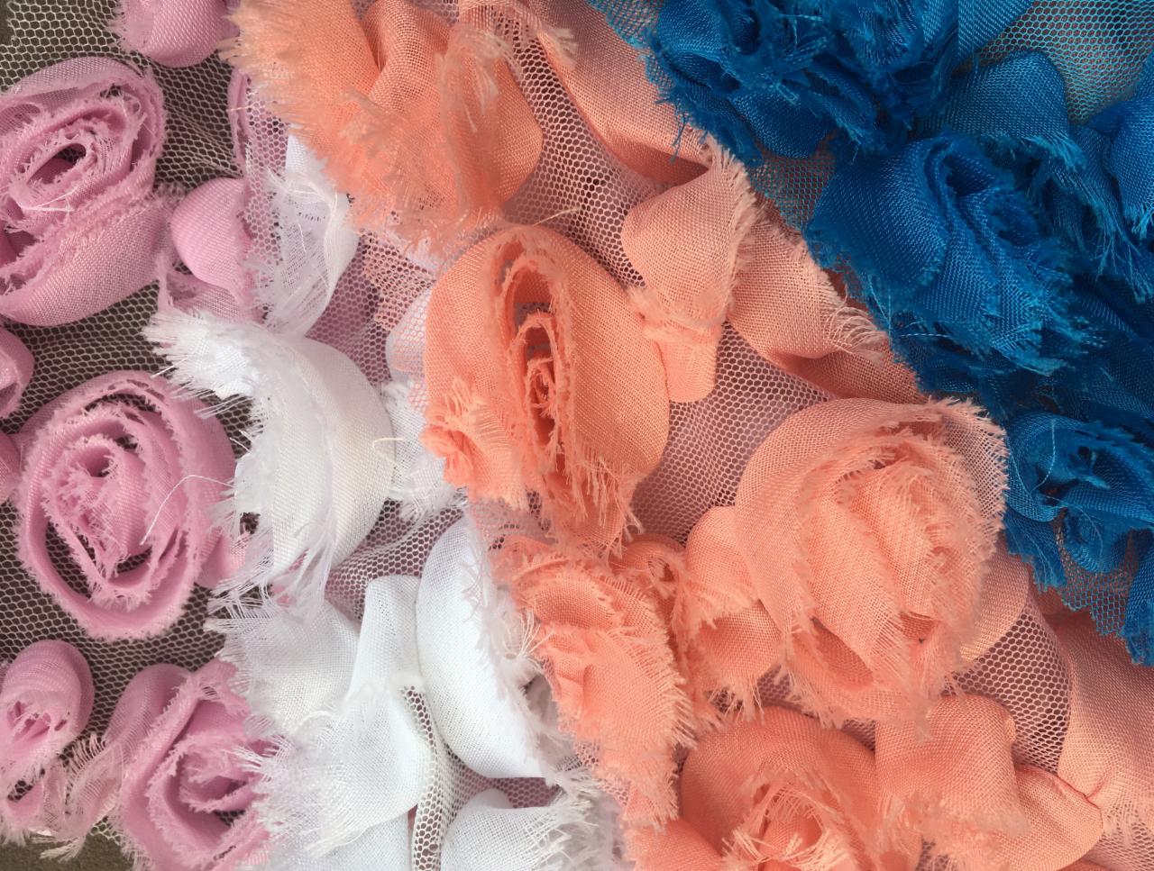 Różnokolorowe, tekstylne różyczki (różowe, białe, brzoskwiniowe i niebieskie) na siatce, makro.