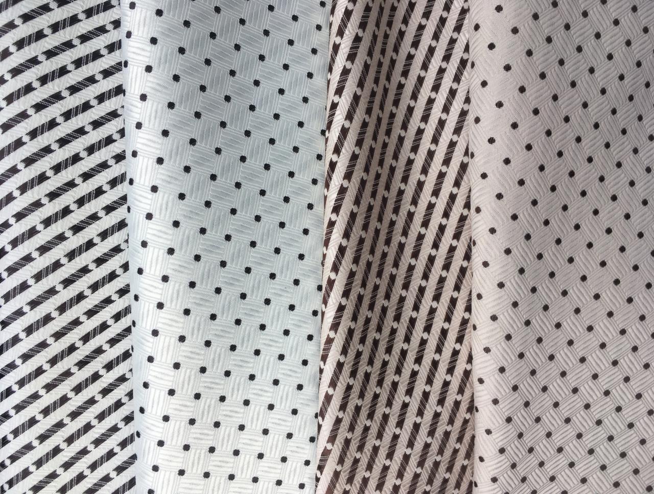 Próbki tkanin z różnymi wzorami: czarno-białe paski diagonalne, biała tkanina w czarne kropki z fakturą siatki, brązowo-białe paski diagonalne i beżowa tkanina w brązowe kropki z fakturą siatki.