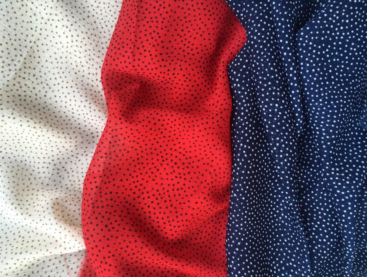 Trzy próbki tkanin: biała w brązowe kropki, czerwona w czarne kropki i granatowa w białe kropki, ułożone obok siebie, tworząc kontrast kolorów i wzorów.