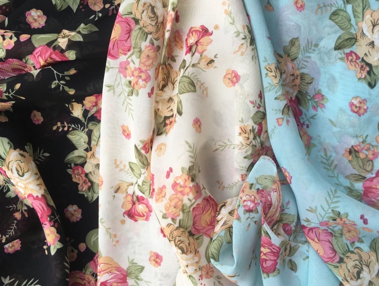 Trzy próbki zwiewnych tkanin w kwiatowe wzory: czarna, kremowa i błękitna, ułożone obok siebie.