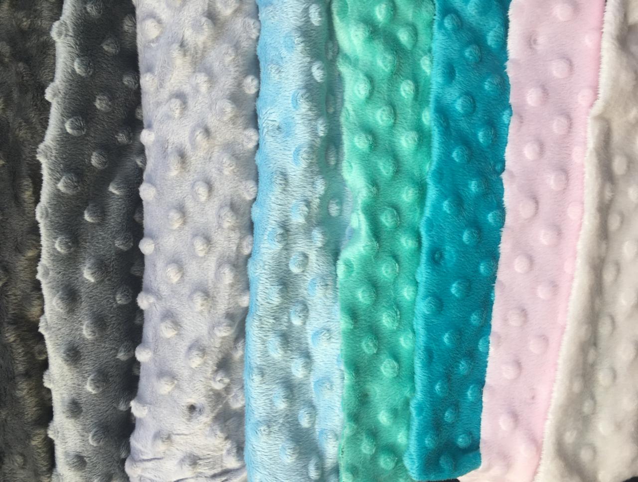 Próbki tkanin minky w odcieniach szarości, błękitu, turkusu, różu i bieli, z charakterystycznymi wypukłymi kropkami.