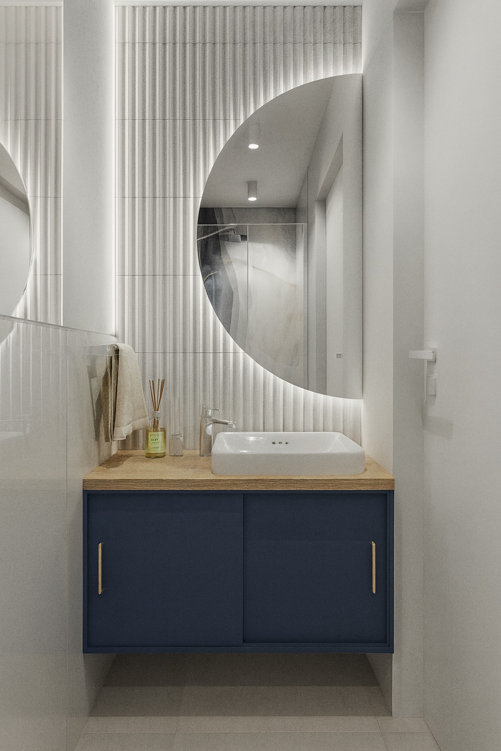 Nowoczesna łazienka z okrągłym lustrem podświetlanym LED, białą umywalką nablatową i szafką w odcieniu granatu. Na blacie dyfuzor zapachowy. Minimalistyczny design i eleganckie wykończenie.