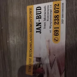 Wizytówka firmy JAN-BUD z usługami budowlano-remontowymi, numerem telefonu i adresem, leżąca na drewnianym podłożu.