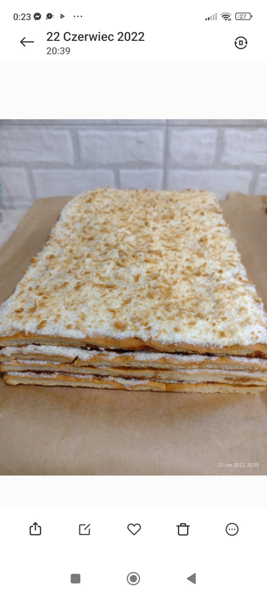 Miodownik: wielowarstwowe ciasto z kremem i posypką, na papierze do pieczenia, na tle ceglanej ściany. Widok z bliska, ukazujący strukturę ciasta.