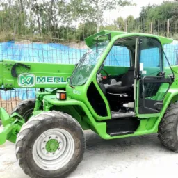 Jasnozielona ładowarka teleskopowa marki Merlo na placu budowy, widoczna z boku, z dużymi oponami i kabiną operatora.