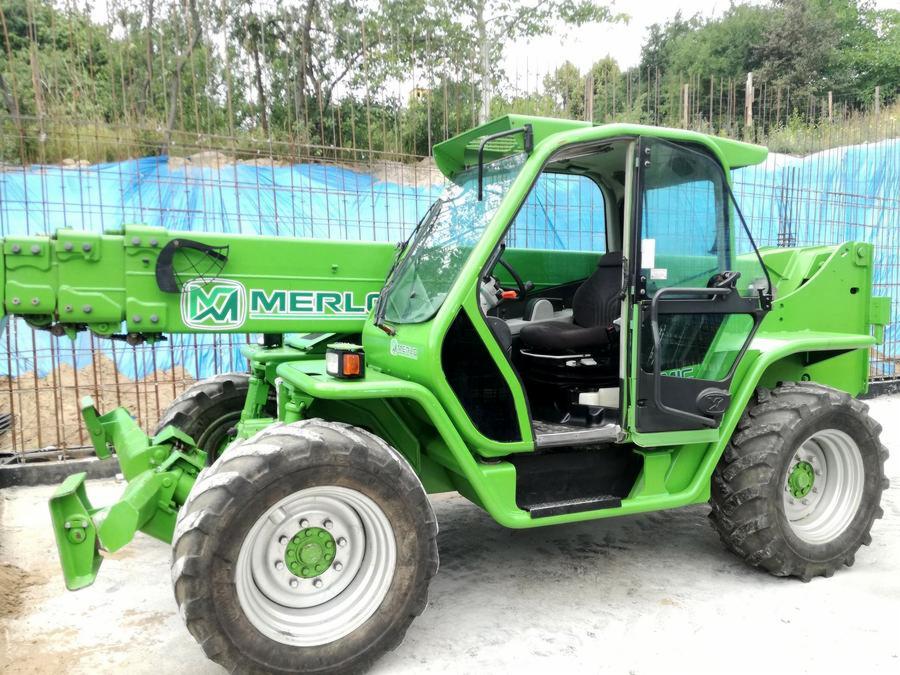 Jasnozielona ładowarka teleskopowa marki Merlo na placu budowy, widoczna z boku, z dużymi oponami i kabiną operatora.