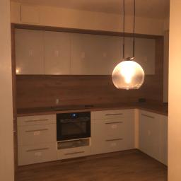 TOM BIN-REMONTY MIESZKAN POD KLUCZ - Nowoczesna kuchnia z drewnianą podłogą i jasnymi szafkami, oświetlona kulistą lampą wiszącą, z widocznym piekarnikiem i blatem.