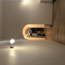 TOM BIN-REMONTY MIESZKAN POD KLUCZ - Ściana z zamontowanym lustrem w kształcie łuku podświetlonym ledami, widoczne odbicie dwóch osób, na podłodze panele, lampka na ścianie.