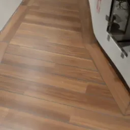 Ukończona podłoga z paneli imitujących drewno, ułożona wzdłuż ściany, z widocznym fragmentem zabudowy meblowej z boku.