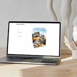 Laptop wyświetla portfolio online Magdaleny Sobolskiej, z kolażem graficznym zawierającym architekturę i jedzenie, obok rzeźba i narzędzia ceramiczne na drewnianym biurku.