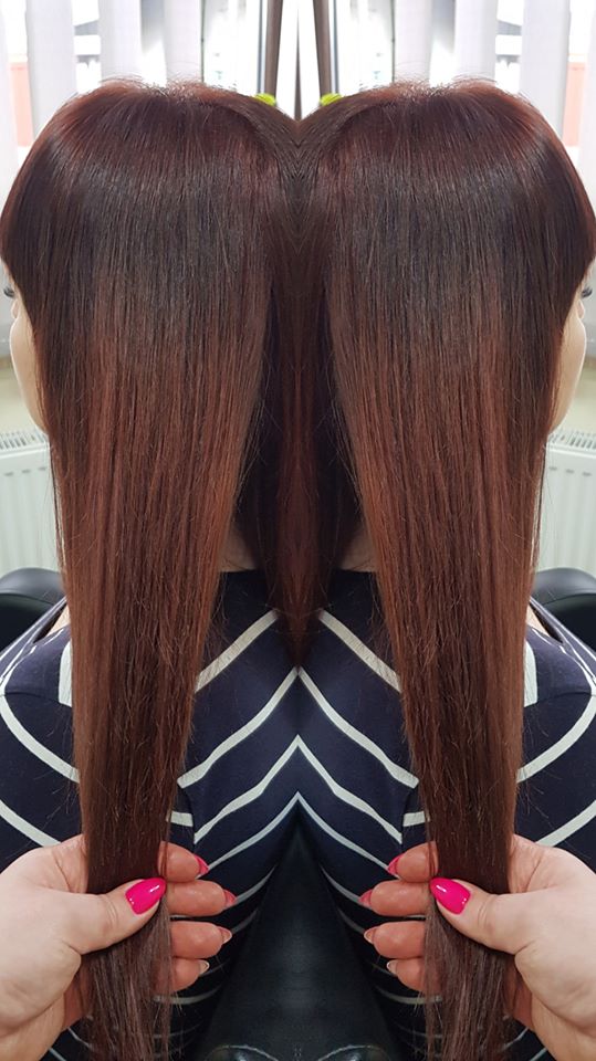 Proste, lśniące włosy w odcieniu mahoniu, przedłużone do pasa, trzymane w dłoniach z jaskrawym różowym manicure.