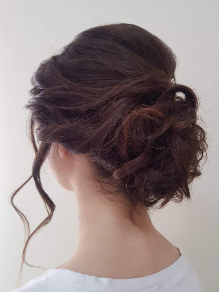 Upięcie z ciemnych włosów z pojedynczym, luźnym pasmem opadającym na szyję, widok z tyłu na jasnym tle.