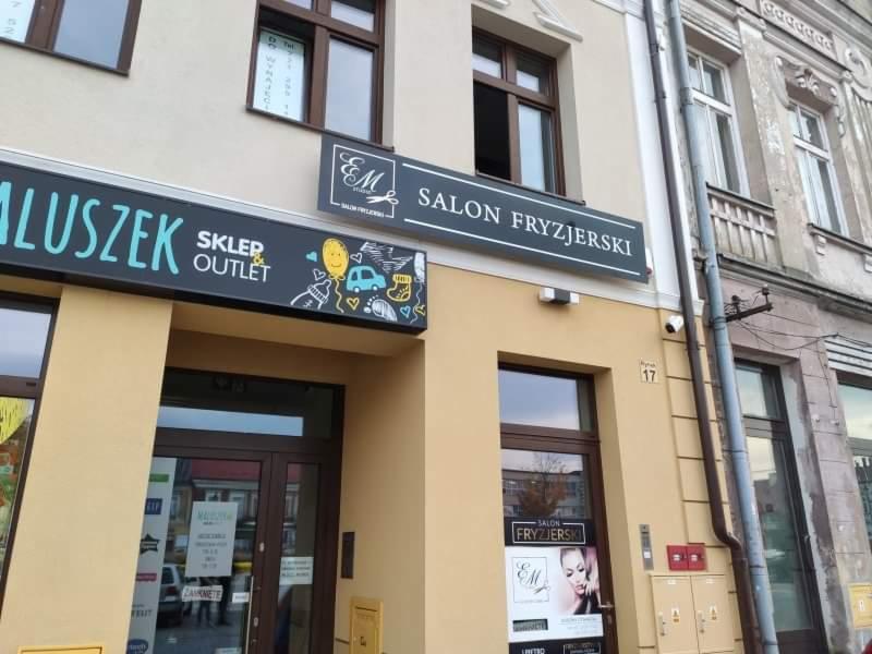 Fasada budynku z szyldami: 'Salon Fryzjerski' z logo oraz 'Sklep Outlet' z dziecięcymi rysunkami, numer budynku 17.