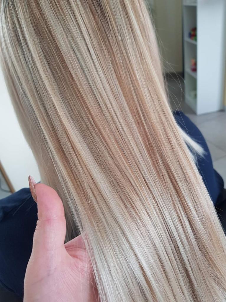 Rozjaśnione, proste włosy w odcieniach blondu i beżu, widoczna dłoń z długim, brokatowym paznokciem.